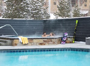 En swimmingpool med en stenvæg, et spabad og et snowboard, der læner sig op ad væggen.