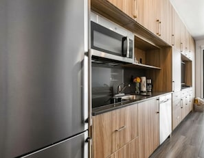 Eine moderne Küche mit Edelstahlgeräten, Holzschränken und einer schwarzen Arbeitsplatte.