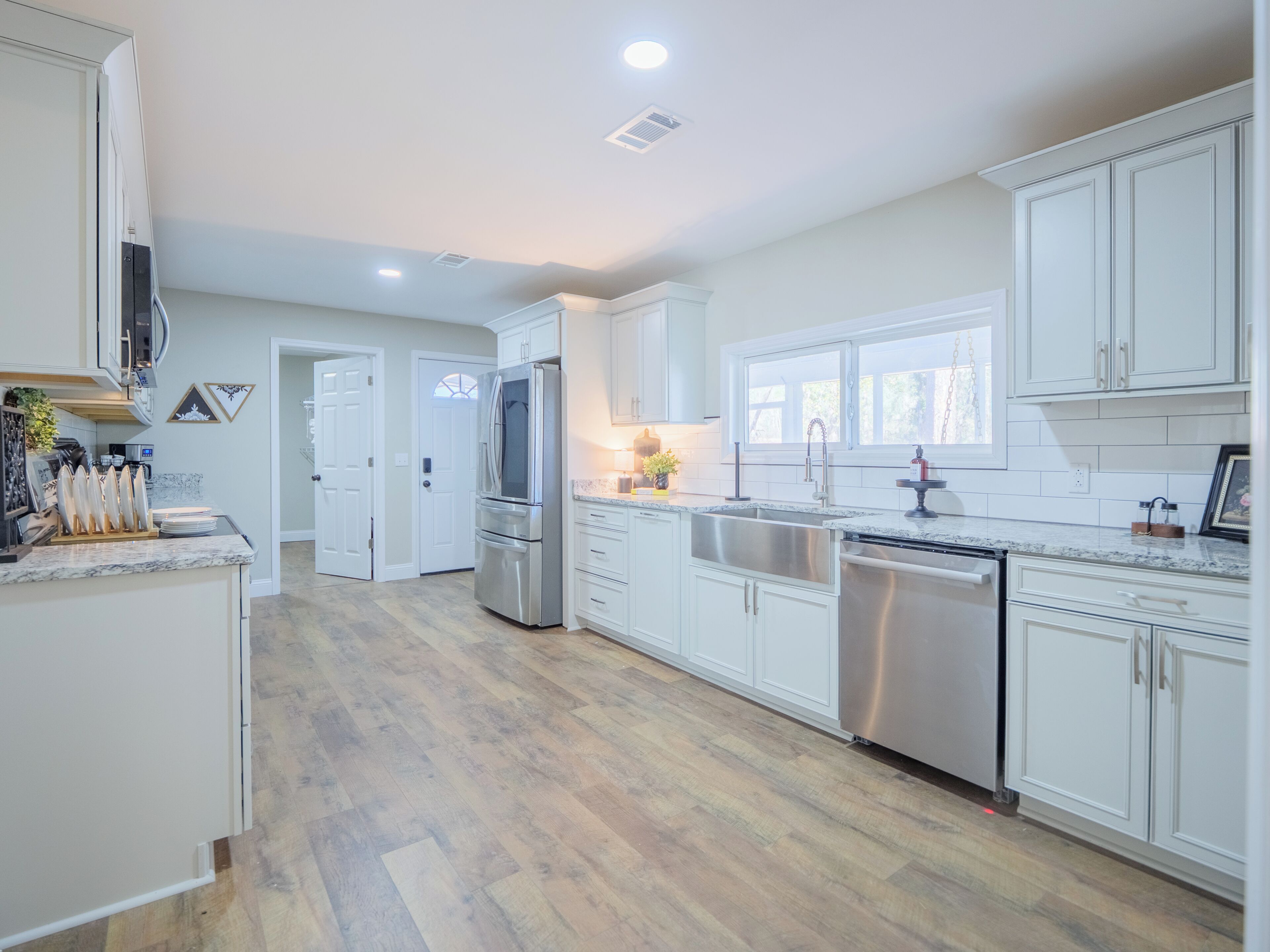 A modern kitchen with white cabinetry, stainless steel appliances, and a wooden floor.