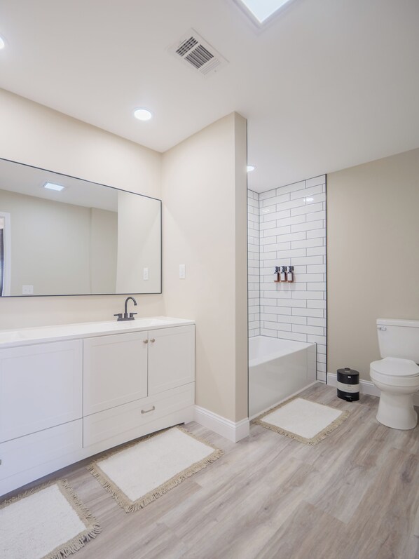 Un baño moderno con un espejo grande, armarios blancos, cabina de ducha de vidrio y un inodoro.