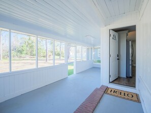 Eine überdachte Veranda mit einer Bank, einer zur Innenseite führenden Tür und einer Fußmatte mit dem Schriftzug 'HELLO'.