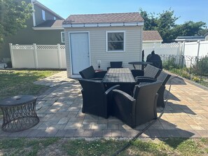 Un patio con una mesa y sillas, un cobertizo pequeño y una valla blanca.