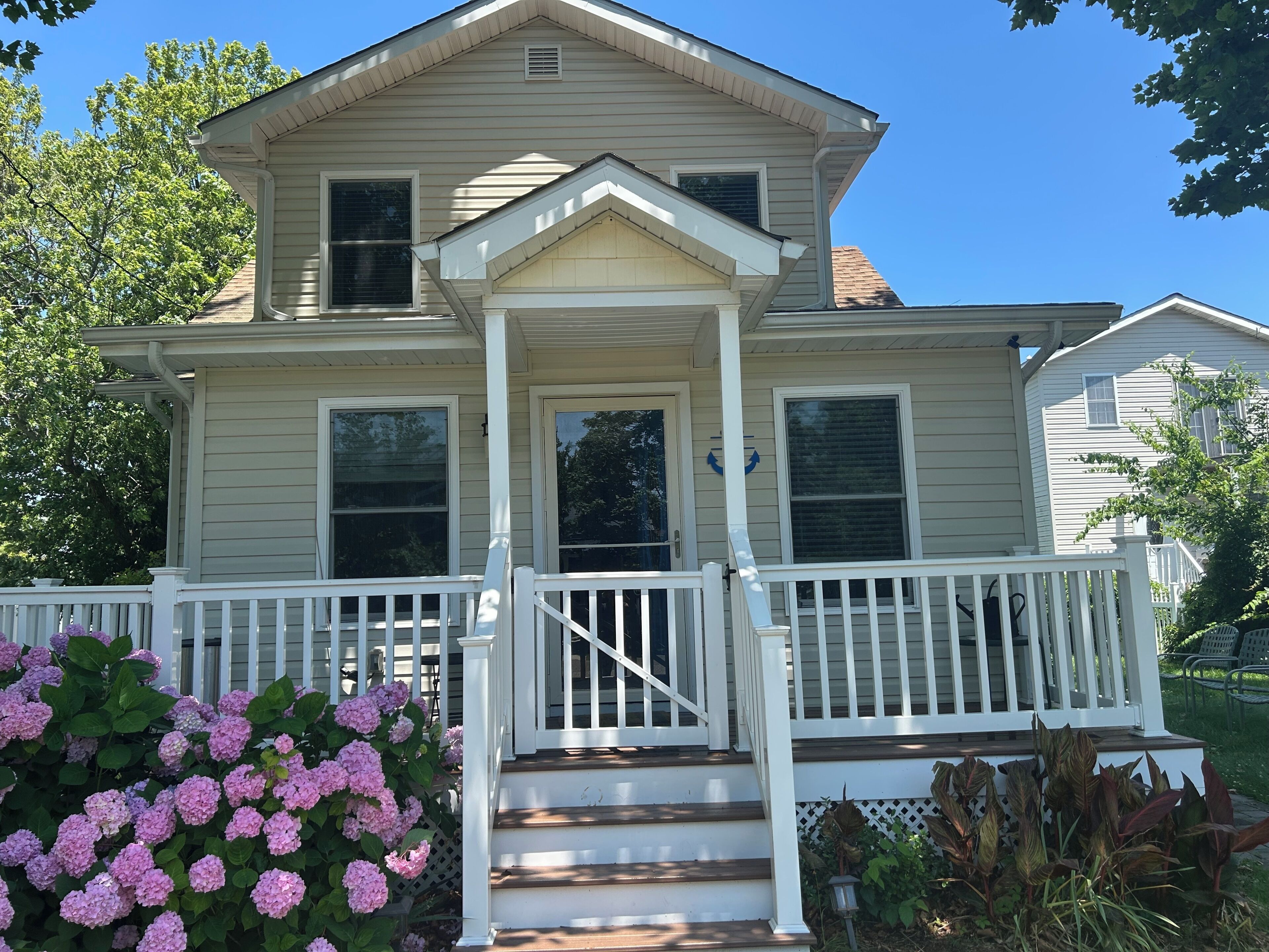 A two-story house with a front porch, a set of stairs leading to the entrance, and a small garden with hydrangea bushes.