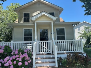 A two-story house with a front porch, a set of stairs leading to the entrance, and a small garden with hydrangea bushes. - 2-bedroom house in fantastic Lower Township back yard and patio (Lower Township)