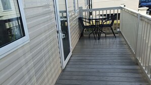 Un terrazzo in legno con tavolo e sedie, una porta scorrevole in vetro e una ringhiera bianca.