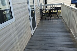 A wooden deck with a table and chairs, a sliding glass door, and a white railing. - cozy 2 bedroom caravan golden sands (Rhyl)