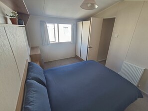A bedroom with a bed, a radiator, a window with curtains, and a door.