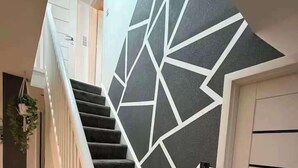 A staircase with a geometric pattern on the wall, white railings, and a door on the right.