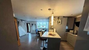 A modern kitchen with a central island, a dining area with chairs, and a staircase leading to another level.