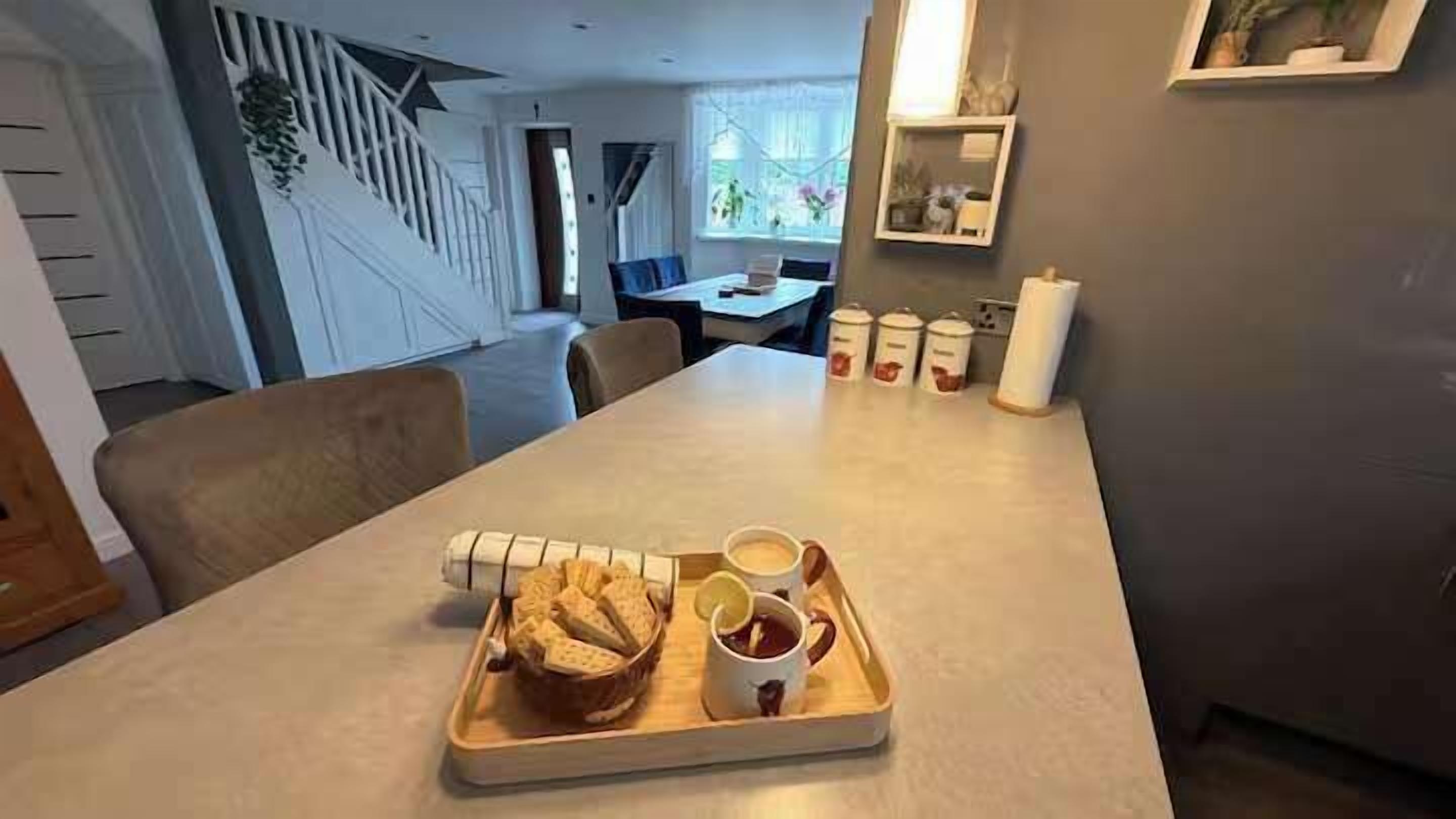 A dining area with a table set for two, a tray with bread and a cup, and a staircase in the background.