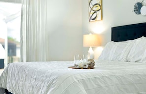 Ein ordentlich bezogenes Bett mit weißer Bettdecke und Kissen, ein Nachttisch mit Lampe und Dekoration, sowie ein Wandbild über dem Bett.