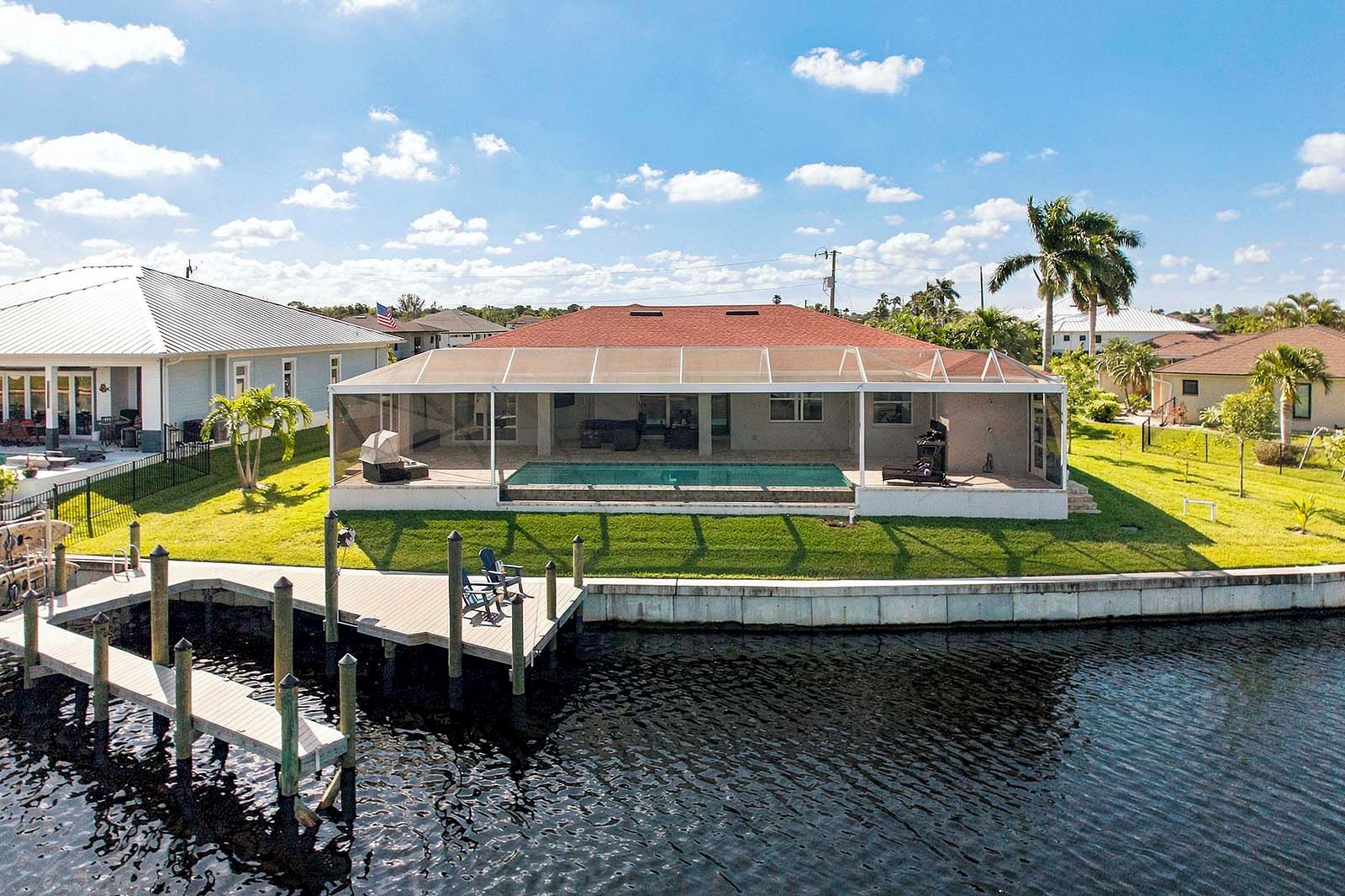 A waterfront property with a covered pool, a dock, and a well-maintained lawn.