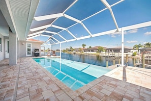 Ein Pool mit überdachtem Patio-Bereich, Blick aufs Wasser und einem wolkenlosen Himmel.