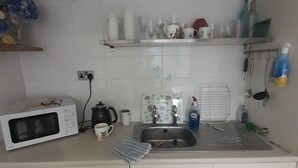 A kitchen with a microwave, sink, and various kitchen items on the counter. - Inviting 1-Bed Cottage in Pontypridd (Pontypridd)
