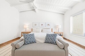 A bedroom with a bed, two bedside tables, a ceiling fan, framed artwork, and a window with blinds. - 7BR Beach House with Firepit, Oceanview Patio and Balcony (Newport Beach)