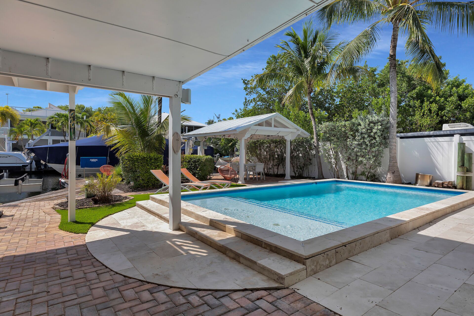 A swimming pool with a covered patio area, a boat dock, and lush greenery.