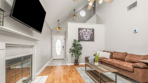 A modern living room with a fireplace, a brown sofa, a coffee table, and a mounted TV. - Cozy Urban Retreat (Pensacola)