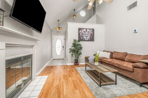A modern living room with a fireplace, a brown sofa, a coffee table, and a mounted TV. - Cozy Urban Retreat (Pensacola)