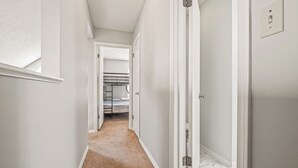 A narrow hallway with white walls and a carpeted floor leading to a bedroom with a bed and a wardrobe. - Cozy Urban Retreat (Pensacola)