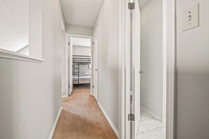 Ein schmaler Flur mit weißen Wänden und Teppichboden, der zu einem Schlafzimmer mit Bett und Kleiderschrank führt.
