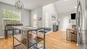 A modern living room with a dining area, wooden flooring, a chandelier, and a fireplace. - Cozy Urban Retreat (Pensacola)