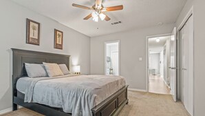 A bedroom with a bed, ceiling fan, and two framed pictures on the wall. - Cozy Urban Retreat (Pensacola)