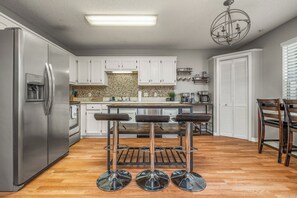 Eine moderne Küche mit weißen Schränken, einem Edelstahlkühlschrank, einer Bar mit Holzstühlen und einer Kristallleuchter.