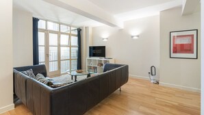 Un salon moderne avec un canapé, une table basse en verre, un téléviseur à écran plat et un tableau abstrait encadré.
