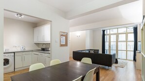 Une cuisine moderne avec des meubles blancs, un lave-linge et un coin repas comprenant une table en bois foncé et des chaises de couleur claire.