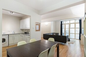 Eine moderne Küche mit weißen Schränken, einer Waschmaschine und einem Essbereich mit einem dunklen Holztisch und hellen Stühlen.