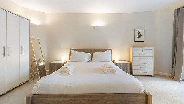 Une chambre d’hôtel avec un lit, une table de chevet, une commode, un miroir et un tableau encadré au mur.