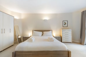 A hotel room with a bed, a nightstand, a dresser, a mirror, and a framed picture on the wall. - GuestReady - Spacious 2bed in Islington (London)