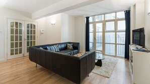 Un salon moderne avec un canapé en cuir noir, une table basse en verre et une grande fenêtre agrémentée de rideaux.