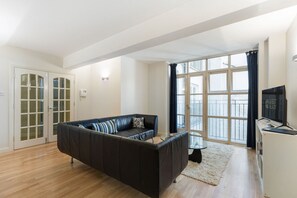 Ein modernes Wohnzimmer mit einer schwarzen Ledersofa, einem Glastisch und einem großen Fenster mit Vorhängen.