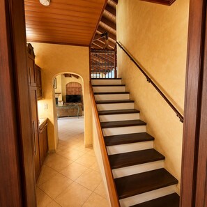 Una escalera de madera con barandilla que lleva a un rellano con vistas a una zona de cocina.