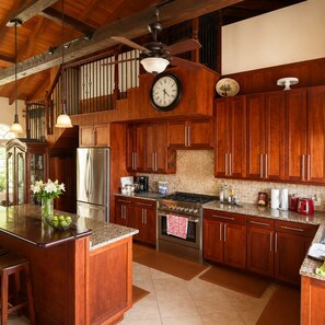 A spacious kitchen with wooden cabinets, a stainless steel refrigerator, a stove, and a large island with a vase of flowers.
