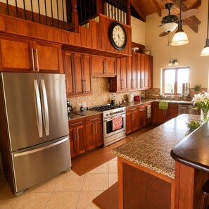 Una cocina con armarios de madera, electrodomésticos de acero inoxidable, un reloj y una ventana con luz natural.