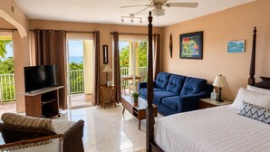 A hotel room with a bed, a TV, a balcony, a sofa, and a ceiling fan.