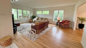 A spacious living room with a large window, a sofa, a wicker chair, and a rug. - Sunny Retreat with Stunning Golf Course Views (Centennial)