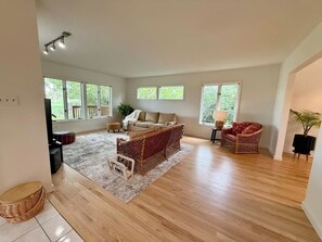 A spacious living room with a large window, a sofa, a wicker chair, and a rug.