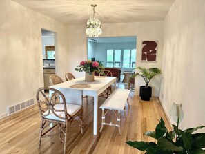 A dining area with a white table, wicker chairs, a bench, and a chandelier.
