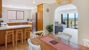 A modern kitchen with a bar area, a dining table with chairs, and a view through an archway to a balcony. - Seaside Escape (Bega Valley)