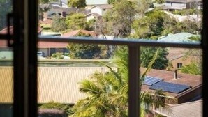 A view through a window of a coastal area with houses, trees, and a clear sky. - Seaside Escape (Bega Valley)