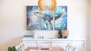 A dining area with a wooden table, white chairs, and a white console table with books and decorative items. - Seaside Escape (Bega Valley)
