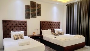 A hotel room with two beds, a nightstand, a wall-mounted artwork, and a large window with curtains.