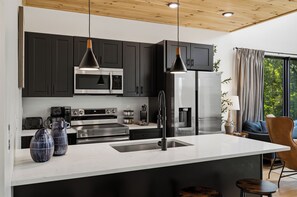 A modern kitchen with dark cabinets, stainless steel appliances, pendant lighting, and a large island with a sink. - Private pool, hot tub, luxury 4 bedrooms, walk in shower (Sevierville)
