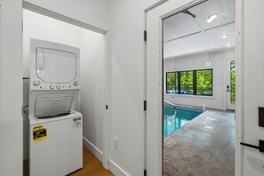 Ein Waschraum mit Waschmaschine und Trockner, ein Poolbereich mit Blick auf Bäume und eine Tür zu einem Raum mit Pool.