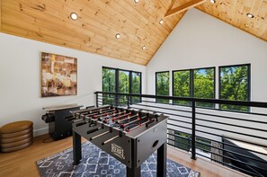 Ein Zimmer mit einem Kicker, einer Couch und einem Fenster mit Blick auf einen Wald.