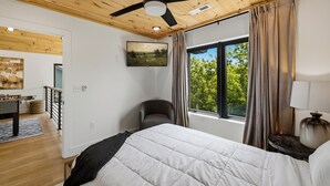 Een slaapkamer met een bed, een plafondventilator, een raam met gordijnen en een schilderij aan de muur.