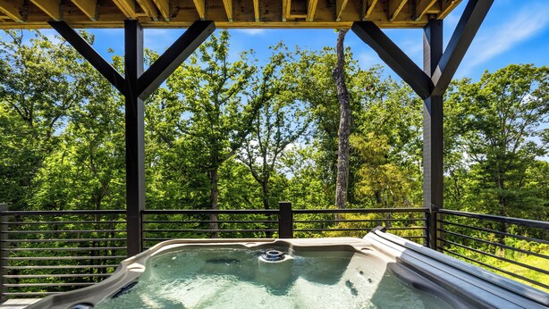 Een hottub onder een houten terras, met uitzicht op een bos.